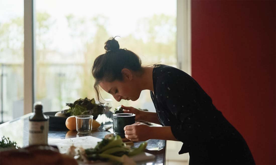 Side view of woman leaning over to smell cooking food in home kitchen